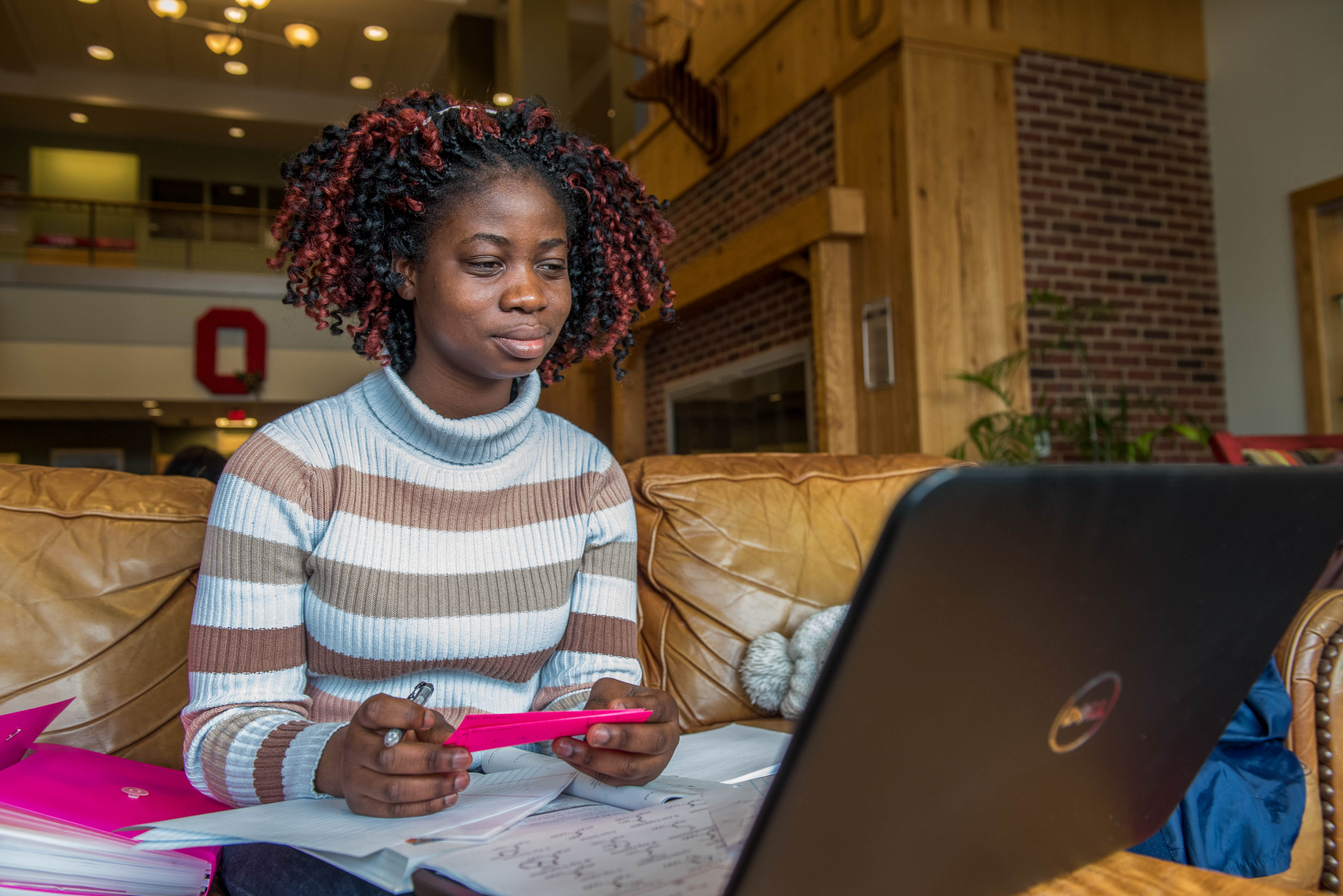 A student is smiling while holding a highlighter and looking at content on her computer.