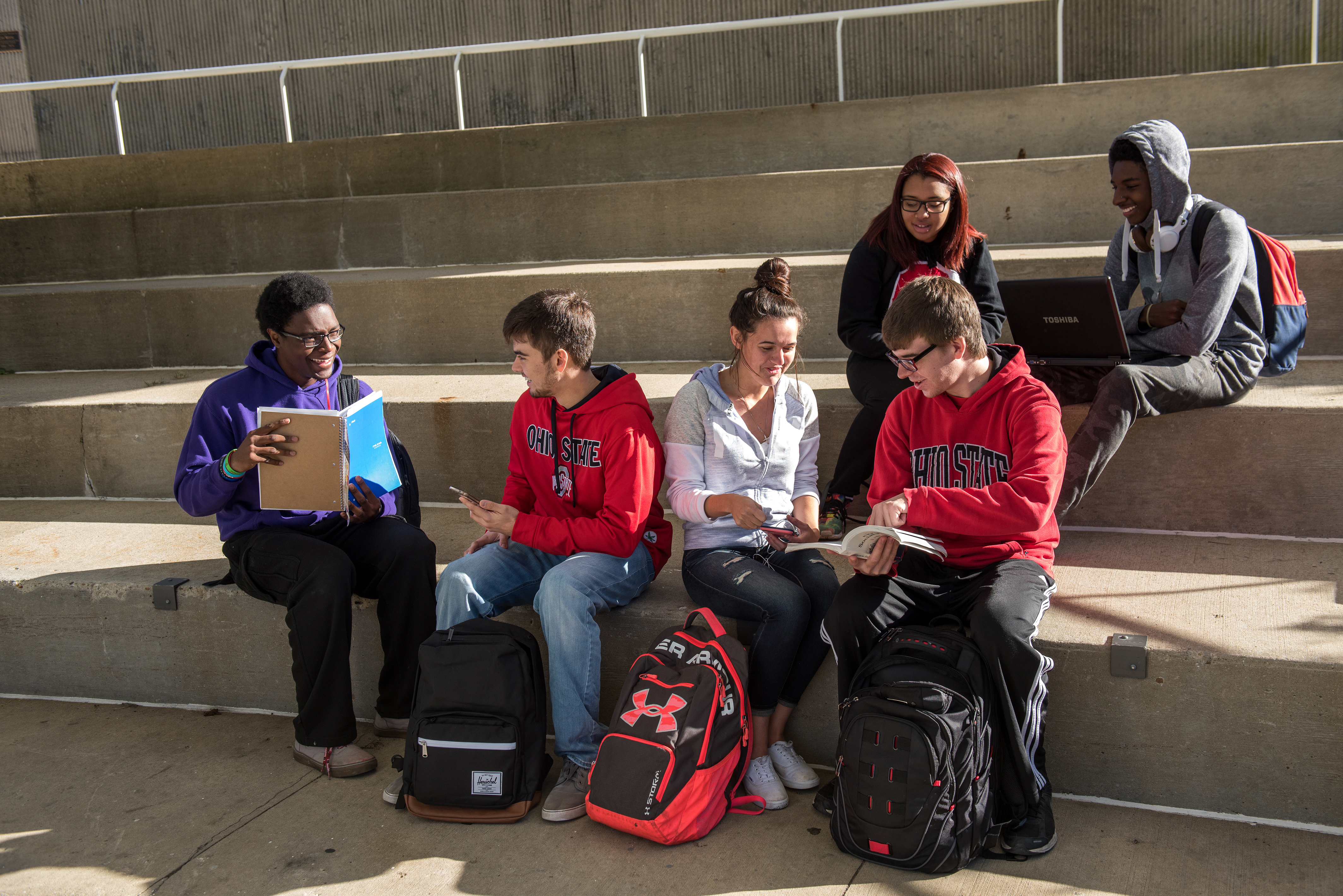 Students are sitting with computer and notebooks smiling and working together.